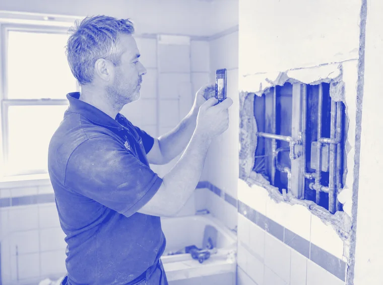 Loodgieter fotografeert met zijn telefoon een geopende wand met koperen leidingen in een badkamer in verbouwing.